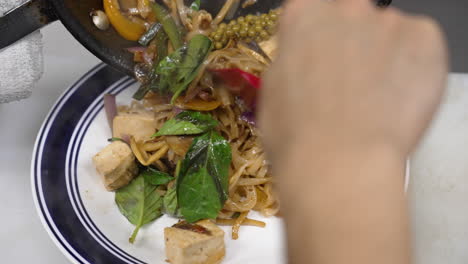 Chef-uses-spatula-to-plate-traditional-tofu-pad-kee-mao-from-steaming-hot-skillet-to-restaurant-plate,-slow-motion-close-up-4K