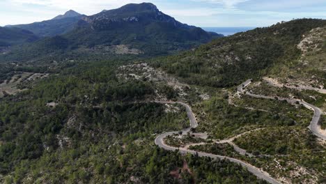 Winding-road-through-green-hills-under-a-clear-sky-in-Mallorca,-aerial-view