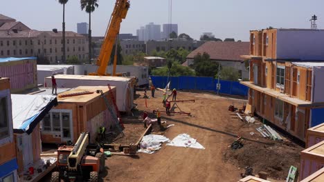 Low-descending-aerial-shot-of-construction-crew-prepping-the-rig-of-a-heavy-duty-lift-crane-at-a-modular-construction-site-in-West-Los-Angeles,-California