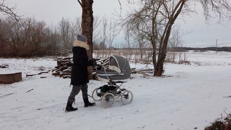 Weibliche-Mutter-Geht-Langsam-Mit-Kinderwagen-Auf-Verschneiter-Landstraße