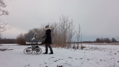 Mother-slowly-push-baby-carriage-on-snowy-countryside-road,-overcast-winter-day