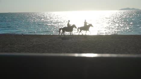 Zwei-Pferde-Laufen-Mit-Ihren-Besitzern-Am-Strand-Entlang