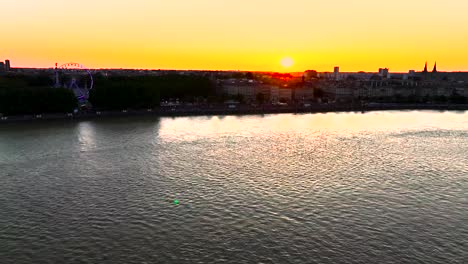 Place-Des-Quinconces,-Bordeaux,-Frankreich,-Ufer-Des-Flusses-Garonne-Mit-Riesenrad,-Beleuchtet-Bei-Sonnenuntergang,-Luftaufnahme