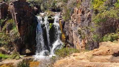 Perspectiva-Aérea-En-Cámara-Lenta-De-Una-Cascada-De-Australia-Occidental-Rodeada-De-Rocas-Y-Arbustos-Australianos.