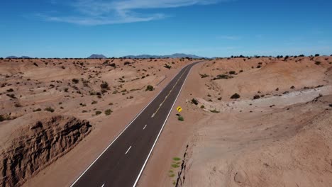 Aerial-follows-clean,-clear-highway-through-red-rock-badland-landscape