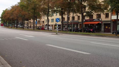 Blue-bus-leaves-stop-on-street-with-car-traffic-in-autumn-Stockholm