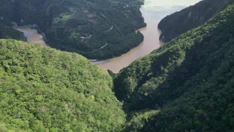 Drone-flying-over-lush-vegetation-with-river-canyon-in-background,-Muchas-Aguas,-San-Cristobal-in-Dominican-Republic