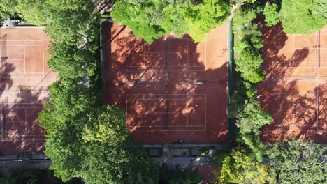 climb-with-drone-camera-down-showing-beautiful-tennis-courts-hidden-in-the-middle-of-many-trees