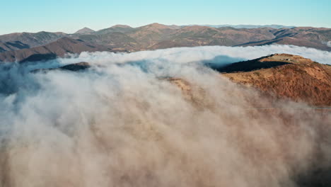 Montañas-Cubiertas-De-Nubes-Con-Picos-Que-Emergen-A-La-Luz-Del-Sol,-Vista-Aérea