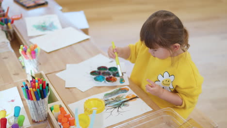 Niedliches-Kind-Mädchen-Kind-Sitzt-Am-Schreibtisch-Mit-Pintbrush-Zeichnen-Und-Malen-Auf-Dem-Papier