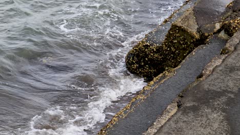 A-close-up-handheld-shot-of-waves-crashing-against-the-stairs-of-a-pier-on-a-lake-in-Auckland,-New-Zealand