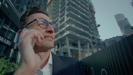 Close-up-shot-of-businessman-talking-on-mobile-phone-happily-talking-employer-while-standing-outside-office-at-daytime