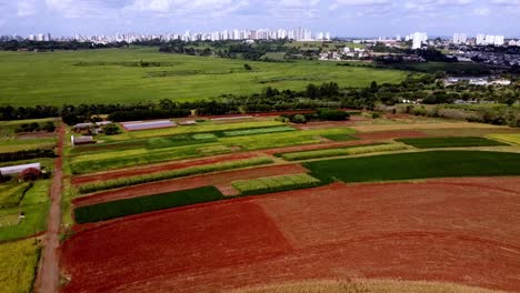 Vista-De-Drones-De-La-Granja-De-Tierras-Agrícolas-Con-La-Ciudad-A-Distancia