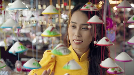 Close-up-of-young-Vietnamese-tourist-in-yellow-dress-touching-souvenirs-in-Hoi-An,-Vietnam