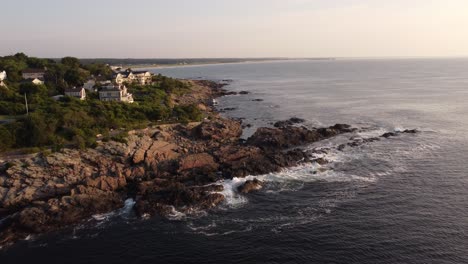 Aerial-of-Ogunquit-Maine-USA-seascape-drone-fly-above-luxury-oceanfront-resort-house-ocean-waves-crash-into-rocky-coastline-beach