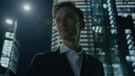 Handsome-executive-young-manager-standing-at-night-in-modern-illuminated-city