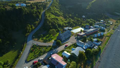 Aerial-drone-fly-above-patrimonial-UNESCO-Church,-Detif-Chiloé-Chilean-Patagonia-Landscape-of-Skyline,-Green-Island-Mountains,-houses-and-south-American-Road-Travel