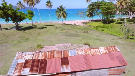Rusty-corrugated-iron-hut-on-tropical-sand-beach-in-the-Caribbean,-aerial