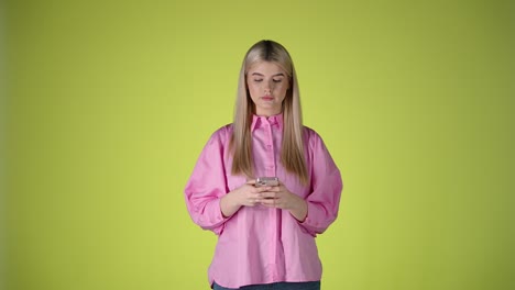 Cute-woman-typing-and-smiling-at-Smartphone,-isolated-yellow-studio-background