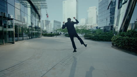 Following-shot-of-a-man-in-suit-happily-walking-outside-office-building-during-evening-time