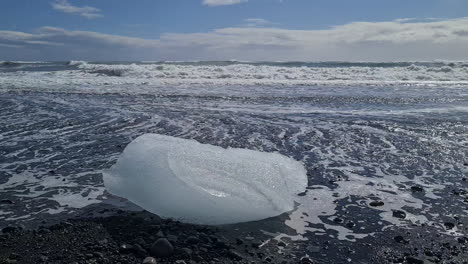 Glacier-Ice-on-Black-Beach-in-Front-of-Sea-Waves,-Global-Warming-and-Climate-Change-Concept