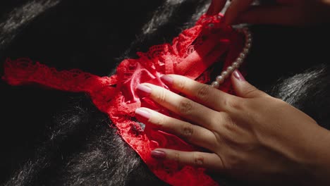 A-woman's-hand-touches-red-lingerie-with-white-pearls