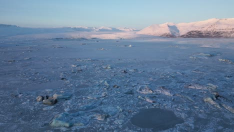 Flug-über-Gefrorenen-Gletschersee-In-Richtung-Der-Berge,-Beleuchtet-Durch-Den-Sonnenuntergang