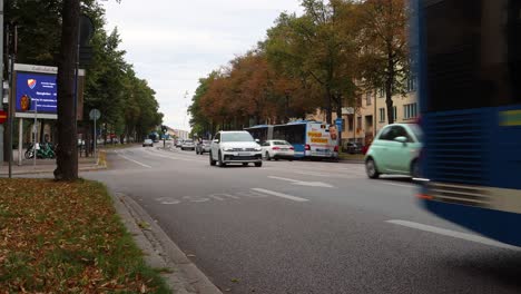 Bus-with-flags-drives-on-trafficked-street-in-autumn-Stockholm,-Sweden