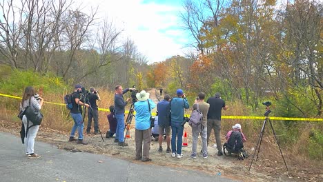 Group-of-people-gathered-at-a-crime-scene-in-the-woods-during-daytime,-some-with-cameras