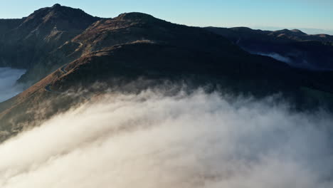Majestic-mountain-peaks-emerging-above-a-dense-layer-of-morning-clouds,-aerial-shot