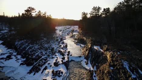 Vista-Increíble-Caída-Del-Río-Rodeada-De-Nieve-Sobre-Rocas-En-La-Hora-Dorada