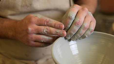 Potter-gently-forming-handmade-edge-of-ceramic-vessel-spinning-on-pottery-wheel