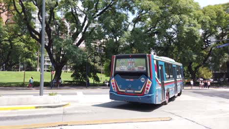 Blauer-Autobus-Fährt-Durch-Die-Straßen-Der-Stadt-Buenos-Aires,-Argentinien,-Im-Städtischen-Grünen-Park-Von-Barrancas,-Belgrano,-Tageslicht-Im-Sommer,-Lateinamerikanische-Stadtstraße