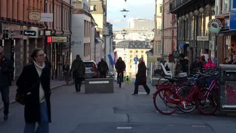 People-on-pedestrian-street-in-Stockholm,-man-rides-bike-past-camera