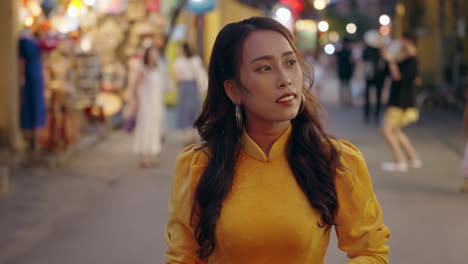 Attractive-Vietnamese-woman-in-traditional-dress-walks-along-night-street-in-Hoi-An-in-slow-motion