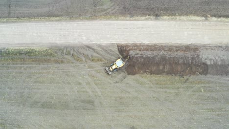 Aerial-top-down-ascend-over-tractor-excavator-dig-drainage-trench-near-road