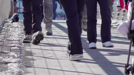 Legs-and-feet-in-winter-clothing-walk-across-a-footbridge-on-a-sunny-but-cold-winter's-day