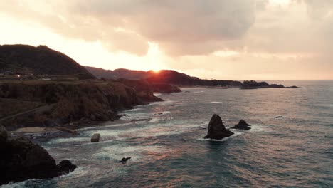 Aerial-fire-golden-skyline-sunset-panorama-at-Japanese-beach,-sea-waves-break-the-shore-rocks-formation-of-Kyotango,-Kyoto-travel-destination-in-Japan,-Asian-summer-drone-shot