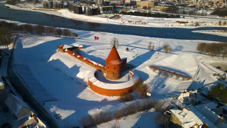 Drone-shot-of-the-historic-old-red-brick-Kaunas-Castle-in-Kaunas-old-town,-near-Neris-river,-in-Lithuania-during-cold-snowy-winter