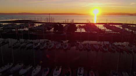 Vuelo-Aéreo-Al-Amanecer-Sobre-Un-Puerto-Deportivo-Al-Amanecer,-En-La-Península-De-California,-Aves-Marinas,-Veleros,-Vistas-Aéreas-Y-Un-Brillante-Sol-Matutino-Reflejándose-En-La-Tranquila-Bahía-De-Sf