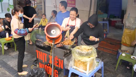 Vibrant-street-food-stall-in-Hanoi-selling-delicious-grilled-meat-skewers,-bustling-atmosphere