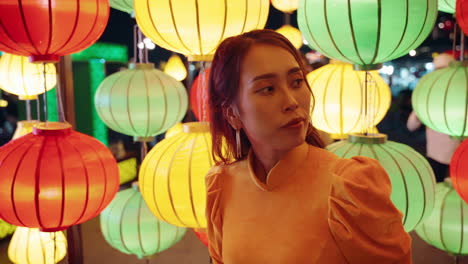 Young-Vietnamese-woman-in-traditional-yellow-outfit-waiting-in-front-of-colorful-lanterns-in-Hoi-An,-Vietnam