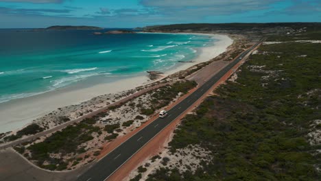 aerial-view-of-a-van-driving-on-twilight-beach-road-near-esperance-on-a-sunny-day-next-to-the-beach-and-ocean-in-Western-Australia