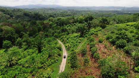 Aerial-view-of-car-slowly-cruising-tropical-forest-on-dust-road