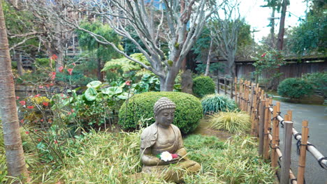 A-4k-slow-motion,-stabilized-video-depicting-a-beautiful-buddha-statue-surrounded-by-flowers,-lush-plants-and-trees-in-a-Japanese-Tea-Garden-in-san-mateo,-california