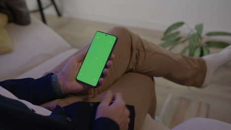 Un-Hombre-Sentado-En-Un-Sofá-Recibe-Un-Teléfono-Celular-Con-Pantalla-Verde