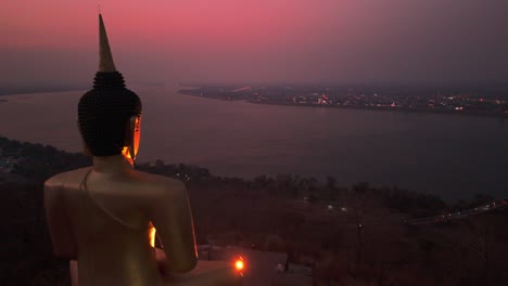 Golden-Beleuchteter-Buddha-Mit-Blick-Auf-Den-Mekong,-Lebendigen-Sonnenuntergang,-Pakse,-Laos