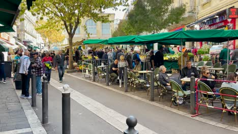 People-walk-and-ride-scooters-by-outdoor-restaurant-in-Marseille