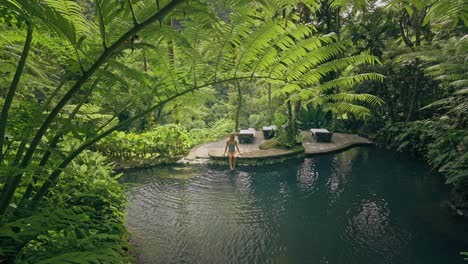 Woman-sitting-on-tropical-pool-edge-in-jungle-creating-ripples-on-water-surface