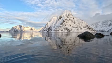 Olstinden-in-Lofoten-at-winter,-low-angle-close-to-sea-surface-with-moving-water